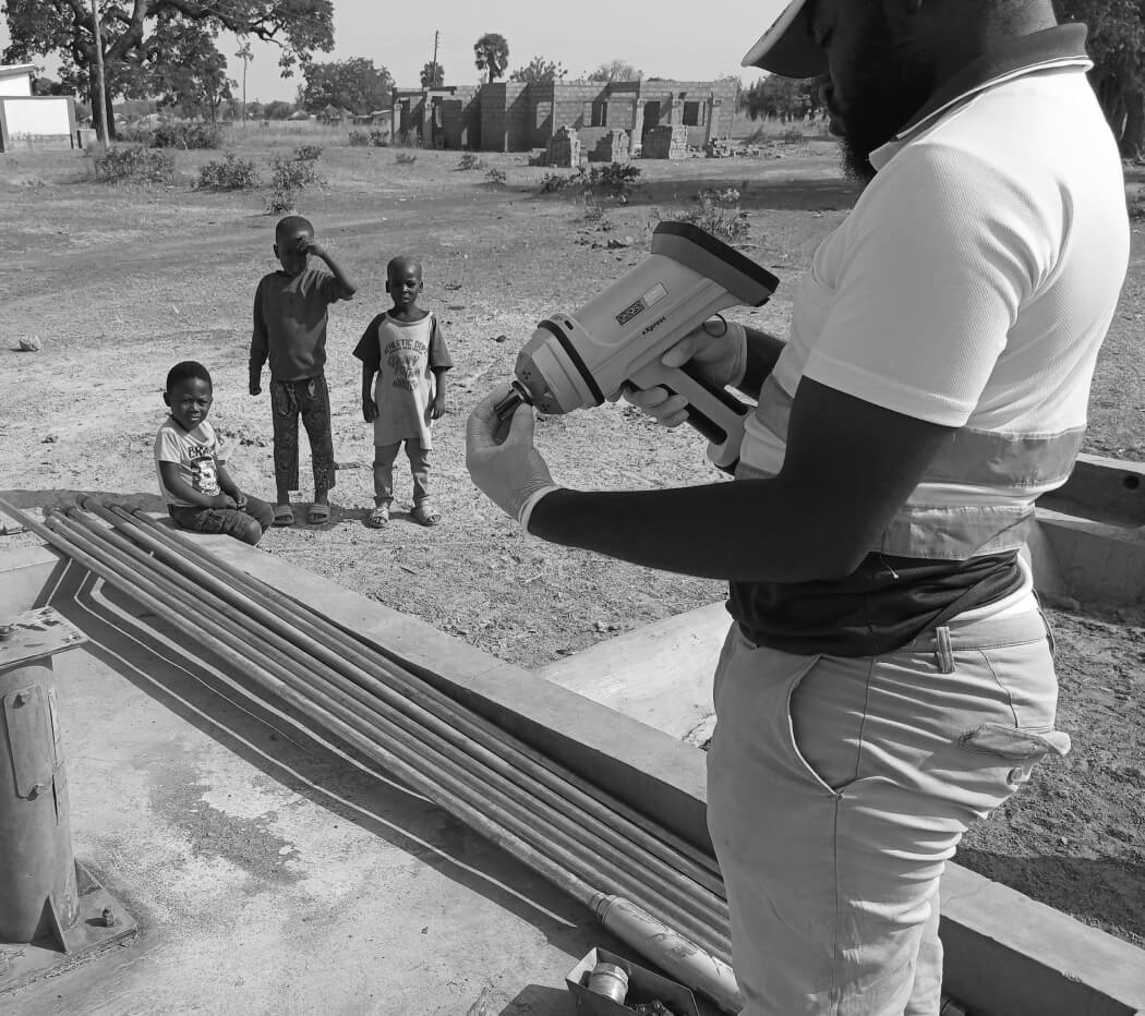 Man installing a new water pump with 3 children watching on.